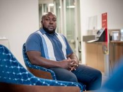 Black male student sitting in chair for posed professional headshot.